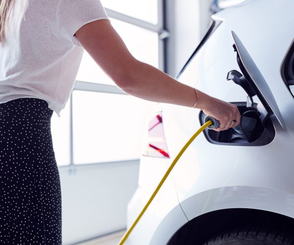 Close Up Of Woman Charging Electric Vehicle With Cable In Garage At Home